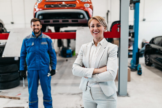 A middle-aged businesswoman in a modern and clean car repair shop is waiting for a mechanic to fix her car.
