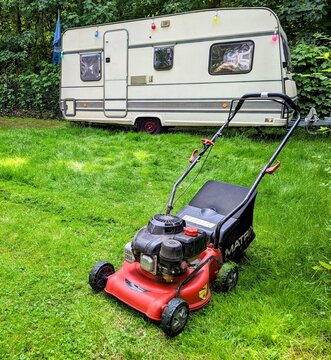 Berlin, 2022: Caravan on a campsite in the forest with a green meadow and a lawn mower