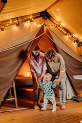 Happy family with lovely baby relaxing and spend time together in glamping on summer evening. Luxury camping tent for outdoor recreation and recreation. Lifestyle concept