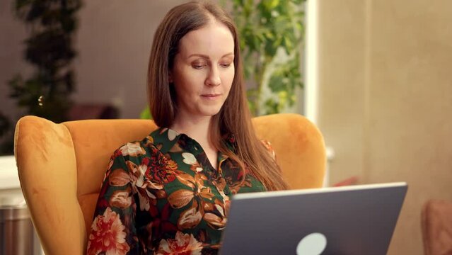 Businesswoman working in business lounge. Entrepreneur sitting on sofa in office lobby using laptop computer to do remote work online. Happy young woman smiling.