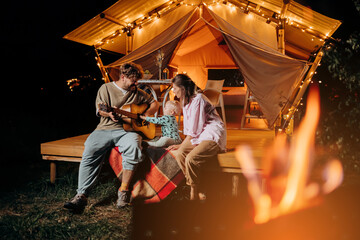 Happy family relaxing and spend time together in glamping on summer evening and playing guitar near...