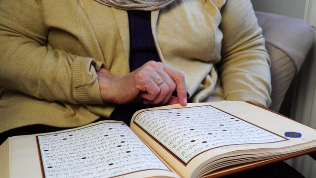 Old Muslim woman reading the Holy Quran at home during Ramadan Month. Old woman wearing white hijab reading the Koran.