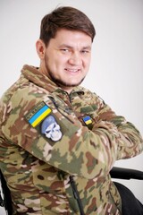 Fototapeta premium Happy positive young man in camouflage uniform soldier sitting in wheelchair and smiling at camera having rehabilitation at clinic for injured veterans