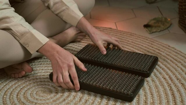 Woman holding open wooden sadhu nail board, touching sharp nails of sadhu board. Trend of self-development over fireplace. Yoga and meditation