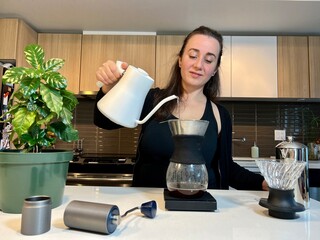 Beautiful young woman with black hair pours water Different professional coffee equipment on the...