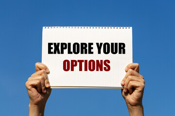 Explore your options text on notebook paper held by 2 hands with isolated blue sky background. This message can be used as business concept about exploring your options.
