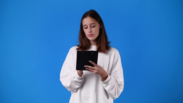 4k video of one girl which thinks and notes something with a pen on tablet over blue background.