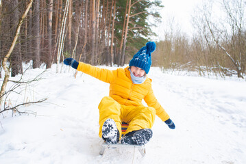 Fototapeta na wymiar happy emotional smiling boy sledding in winter snowy forest