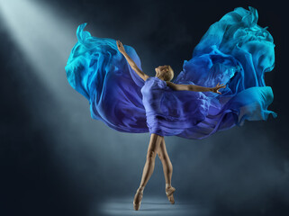 Ballerina in Purple Chiffon Dress on Stage Light Beam. Ballet Dancer in Silk Fantasy Blue Gown. Woman dancing with flying Cyan Fabric as Wings over Dark Background - 579869931