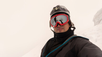 Climber with helmet, headlamp and black jacket taking a selfie on a glacier on a cloudy day