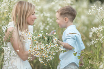 Little cute boy gives his mom a bouquet of daisies. Young gentleman. Lifestyle portrait of mom and son. Family time together. Selective focus