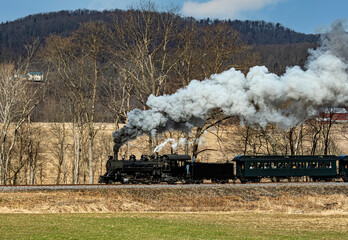 View of a Narrow Gauge Restored Steam Passenger Train Blowing Smoke and Traveling Thru Farmlands on a Winter Day