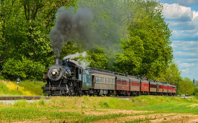 Fototapeta na wymiar View of an Antique Restored Steam Passenger Train Approaching Along a Lone Rail Road Track on a Spring Day