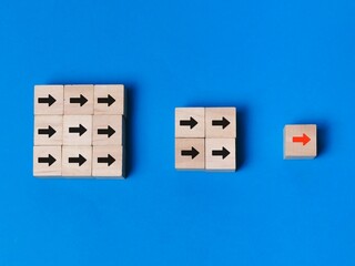 Red arrow leading among black arrows on wooden cubes against blue background.