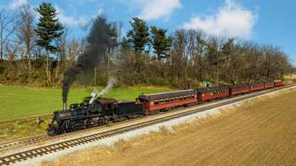 Fototapeta na wymiar A Drone View of a Restored Steam Passenger Train Traveling Thru Farmlands Pulling Up to a Small Station on an Autumn Day