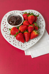 Ripe Strawberries on a Heart-Shaped Plate with Chocolate Dipping Sauce in a Bowl on a Red Background
