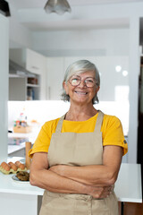 Happy senior 60s lady looking at camera, smiling. Cheerful homeowner woman, food blogger preparing ingredients for dinner. Head shot portrait preparing dinner or lunch..