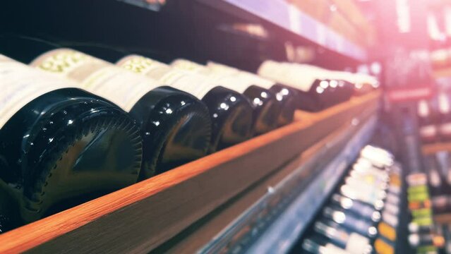 Red wine bottles lie on the wooden shelf of an ABC store or liquor store. Close up shot
