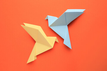 Beautiful colorful origami birds on orange background, flat lay