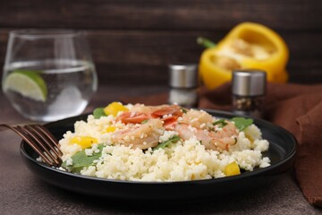Tasty couscous with shrimps, bell pepper and basil on brown textured table, closeup