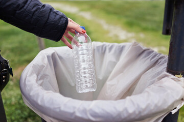Woman throwing plastic water bottle in a public trash can. Plastic waste with recycling concept with only hands visible.