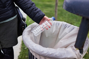 Woman throwing plastic water bottle in a public trash can. Plastic waste with recycling concept with only hands visible.