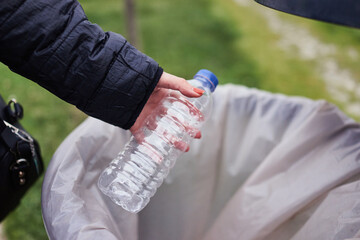 Woman throwing plastic water bottle in a public trash can. Plastic waste with recycling concept with only hands visible.