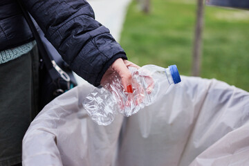 Woman throwing plastic water bottle in a public trash can. Plastic waste with recycling concept with only hands visible.