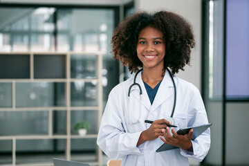 Portrait Of Smiling black Female Doctor Wearing White Coat With Stethoscope holding tablet standing...