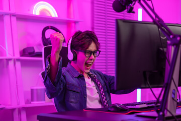 Asian gamer with a happy expression and raised fists in front of a computer screen,Celebrating...