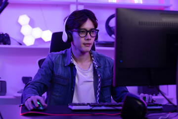 Asian gamer with a happy expression in front of a computer screen, lokking in computer screen and concentrate with online video game. Professional gamer concept © 220 Selfmade studio