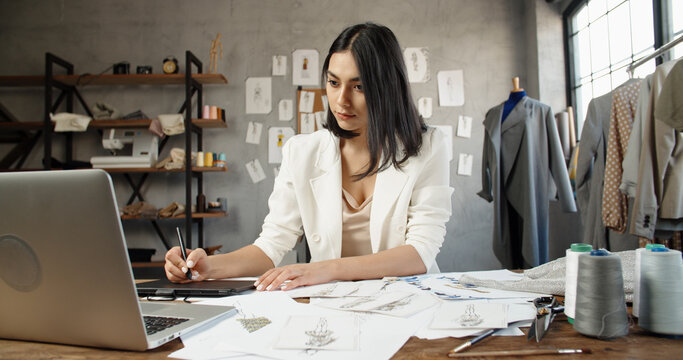 Young Asian woman entrepreneur fashion designer working in studio. Asian female clothing designer is drawing her sketches on graphics tablet, preparing her new collection - fashion, success concept 