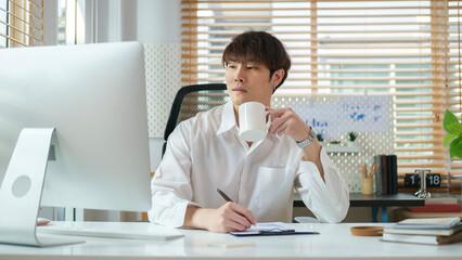 Young businessman drinking coffee and reading online information or email on laptop computer.