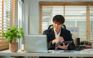 Handsome young businessman using computer laptop while sitting in bright modern office.