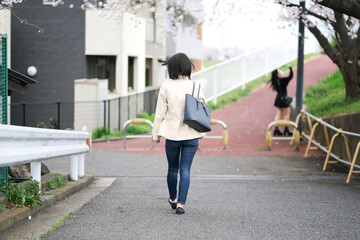 桜の咲く道を歩く女性の後ろ姿