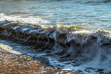 Transparent sea wave. Splashes of waves break on the rocks. Coastal waves. Sea surf on the beach. The power of water on the sea surf. Splashes of sea waves. Spray breaks from powerful waves.