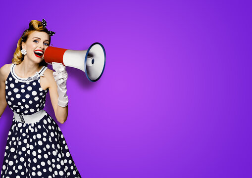 Portrait image of beautiful woman holding mega phone, shout, saying, advertising. Pretty girl in black pin up style dress with mega phone loudspeaker. Isolated violet purple background. Big sales ad.
