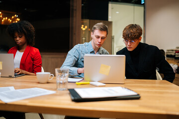 Portrait of young creative business team discussing online project working together on laptop computer at business meeting on modern boardroom. African-American female colleague working nearby.