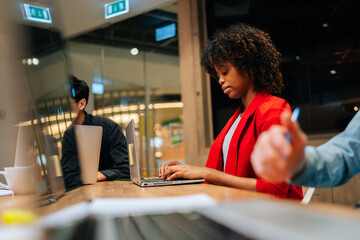 Selective focus of focused African American business woman working typing on laptop sitting at desk during multicultural professional businesspeople working together on research plan in boardroom.