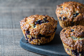 Delicious muffins with blueberries on a wooden table, closeup. Sweet pastries on the board. Fresh cupcakes for breakfast
