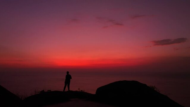 A man stands and takes a selfie against a scene with a red sky..The male silhouette in the sky and sea scene was red on the steep cliff..red sea red sky of twilight background.atmosphere pleasant.