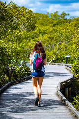 A girl with a colorful backpack walks on a wooden footbridge through unique green mangrove forest - Tinchi Tamba Wetlands Reserve nar Brisbane, Queensland, Australia