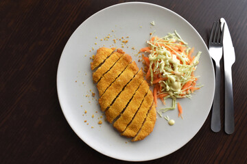 Breaded chicken schnitzel with vegetable salad included carrot and cabbage on a plate. Golden crispy fried chicken. German food.