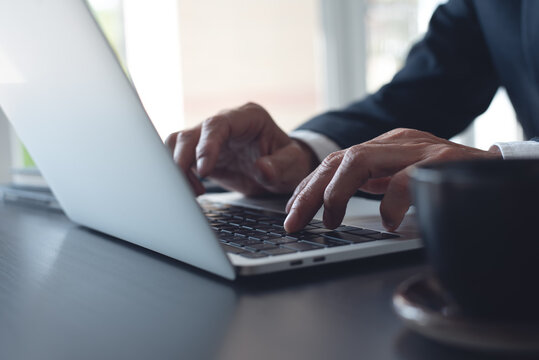 Businessman online working on laptop computer, surfing the internet, networking at modern office, closeup. Business man hand typing ob laptop computer keyboard on office desk