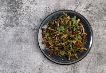 Grilled beef salad with cucumbers, onions, herbs and sesame seeds on a round plate on a dark gray background. Top view, flat lay