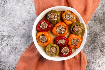 Oven baked stuffed bell peppers with ground beef and rice in a white baking dish on a dark grey background. Top view, flat lay