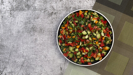 Summer homemade tomato and cucumbers salad on a round plate on a dark gray background. Top view, flat lay