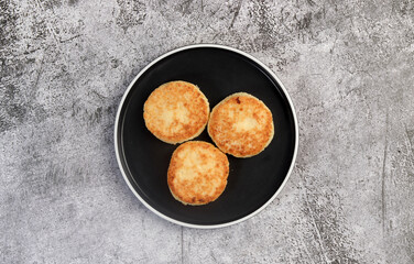 Cottage cheese pancakes on a round plate on a dark grey background. Top view, flat lay