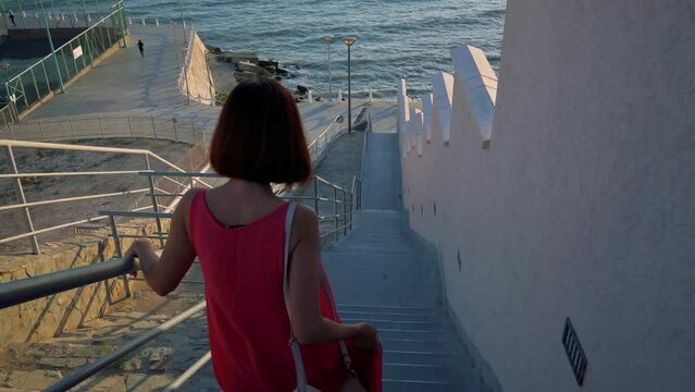 Woman in red dress walking down stairs to the Baltic sea. Woman impressed with the nature. 4k footage UHD 3840x2160 