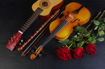 A violin with a bow, a guitar, a pipe, a bouquet of red roses on a black table.